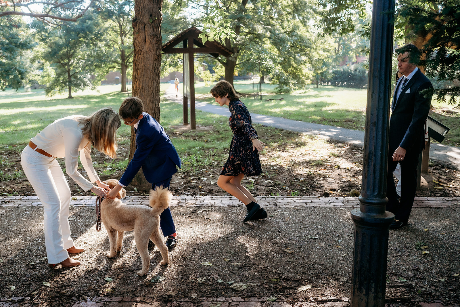 Family adjusts the dog’s leash and gathers together in a sunny park, prepping for a candid photo during their session.