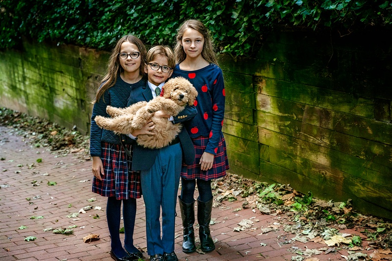 Three kids stand close together as the youngest cradles their puppy, all dressed in school-inspired fall outfits for their family photo session.