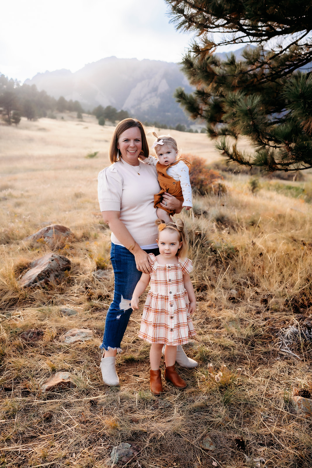 Mom standing with her daughters in a Colorado meadow, framed by fall grasses and mountain views during family photos Denver.