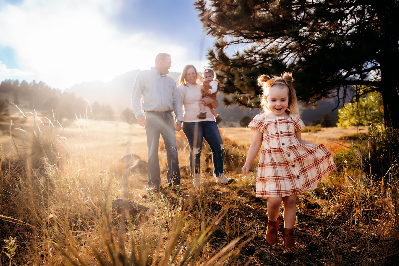 Little girl twirling in her plaid dress while her parents and sister watch with smiles in the background during family photos Denver.