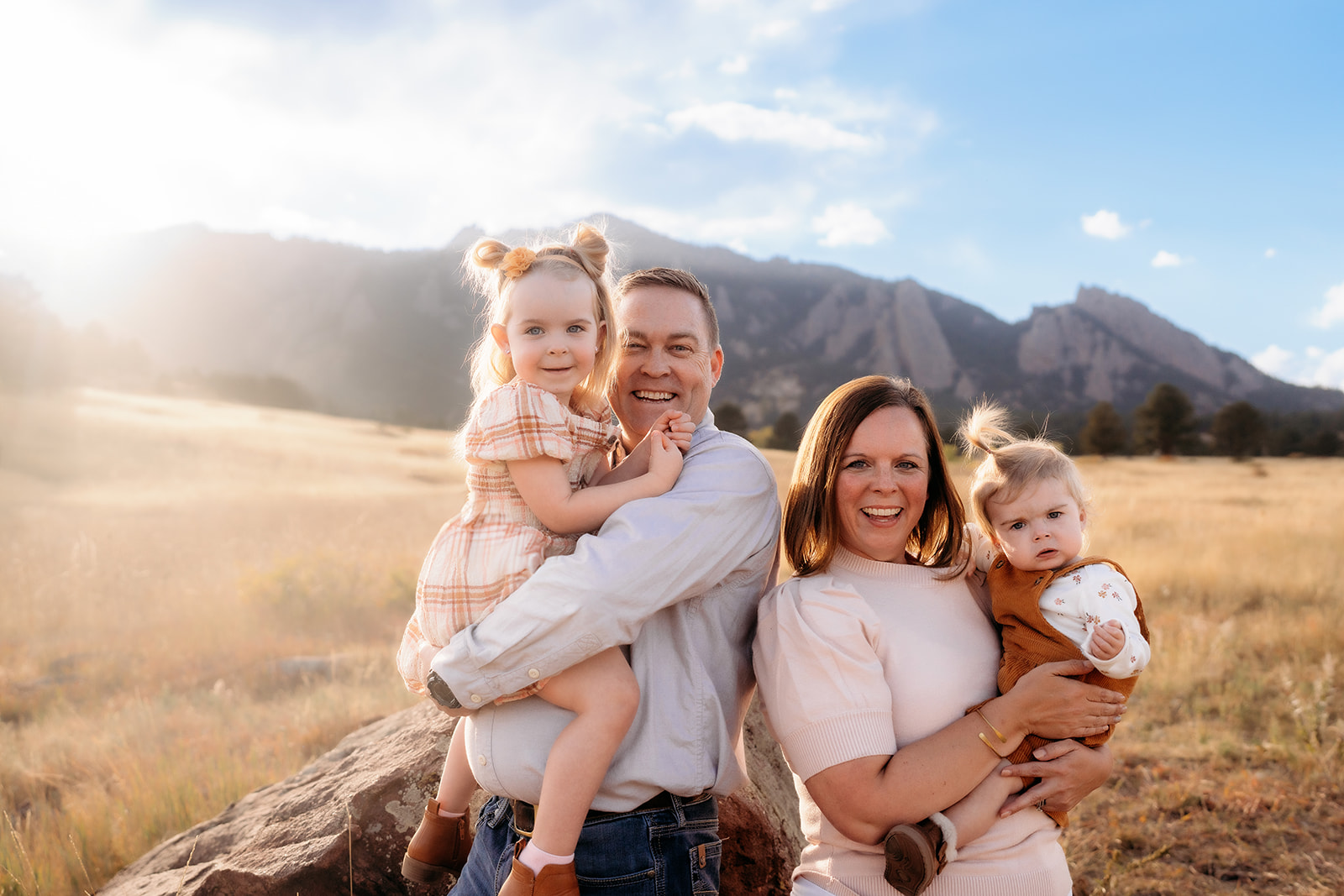 Parents holding their daughters and smiling together in front of the Flatirons during family photos Denver.