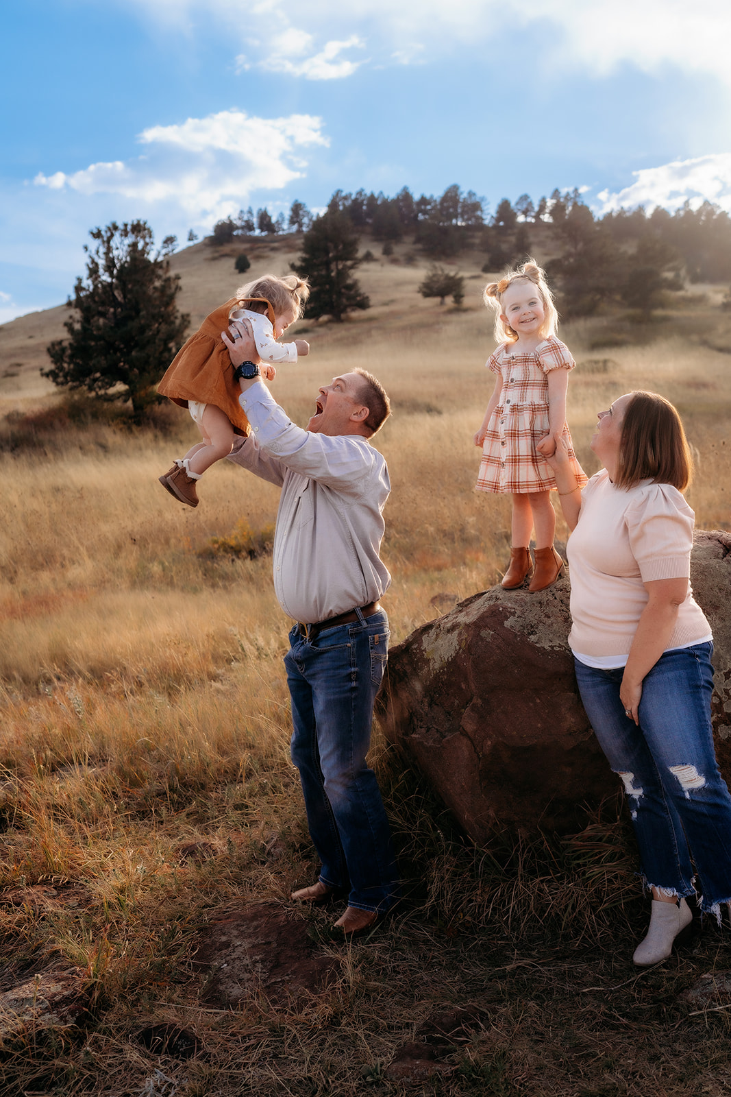 Dad lifts his daughter into the air while the family smiles together in a Colorado meadow.
