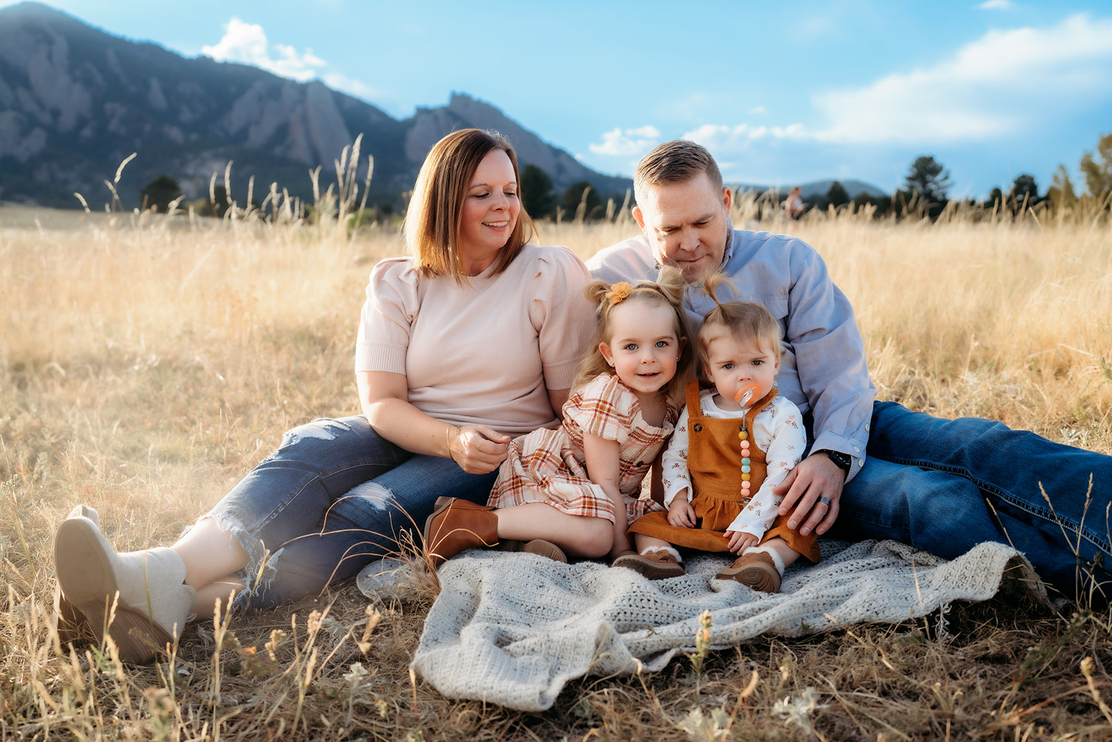 Family sitting close together on a blanket in the grass, enjoying a quiet fall afternoon in Boulder.