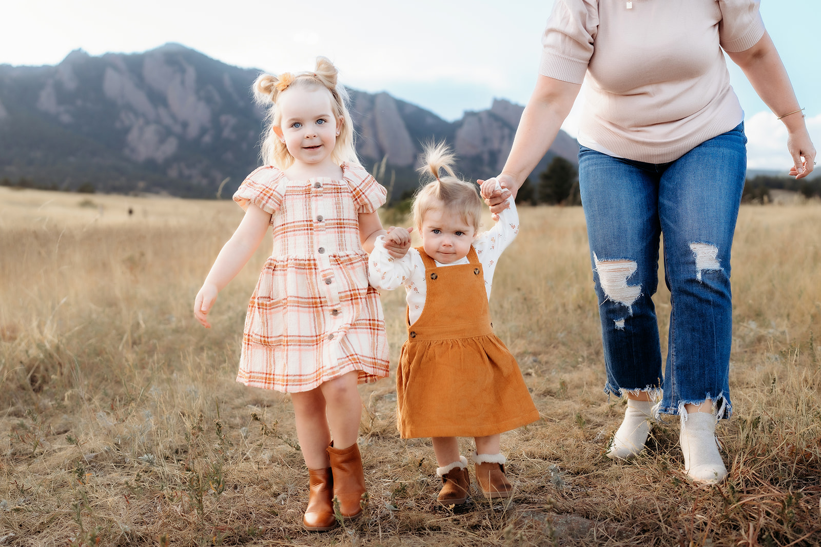 Two little girls holding hands and walking through the grass with their mom during family photos Denver.
