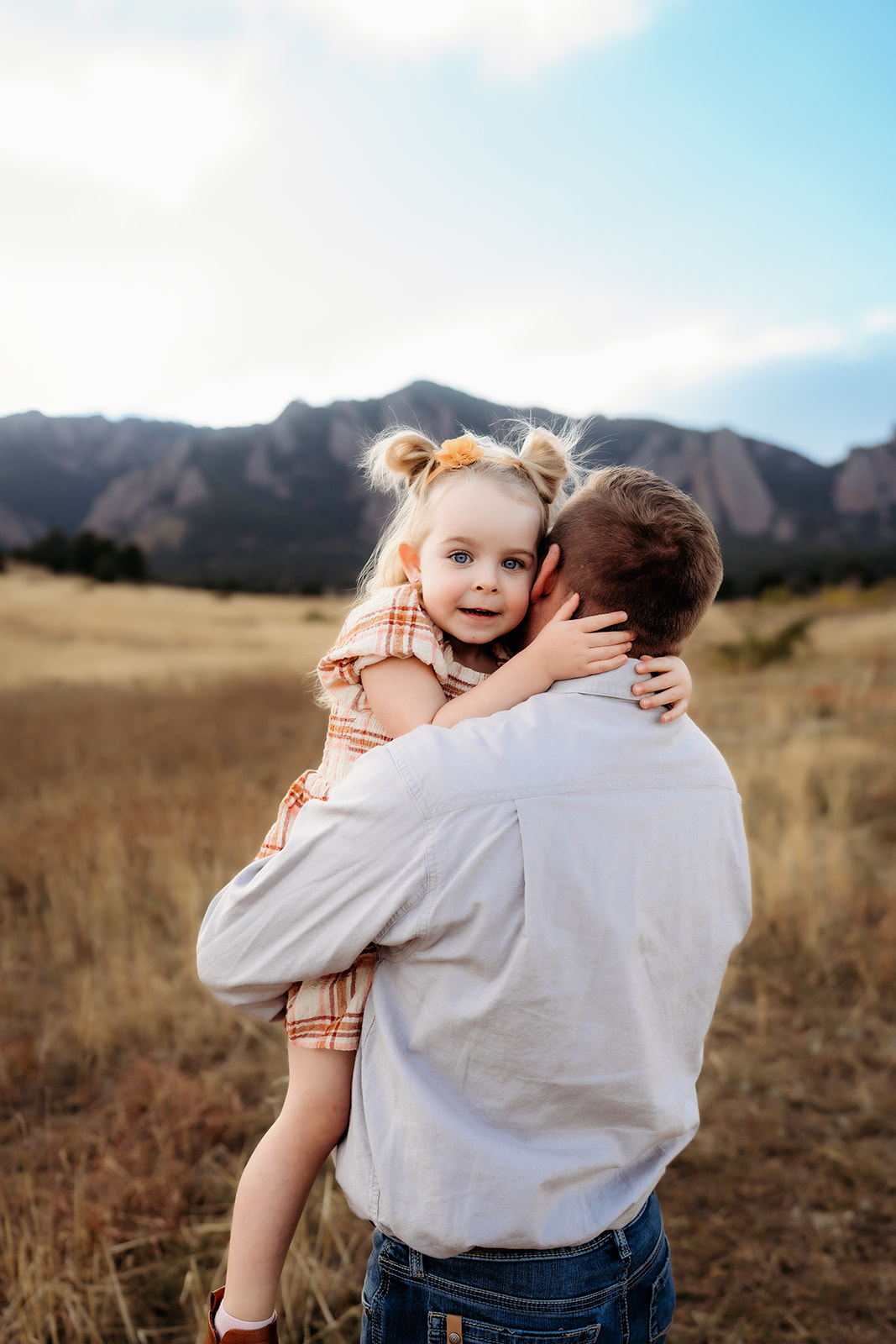 Little girl resting on her father’s shoulder, embraced tenderly with mountains in the distance.