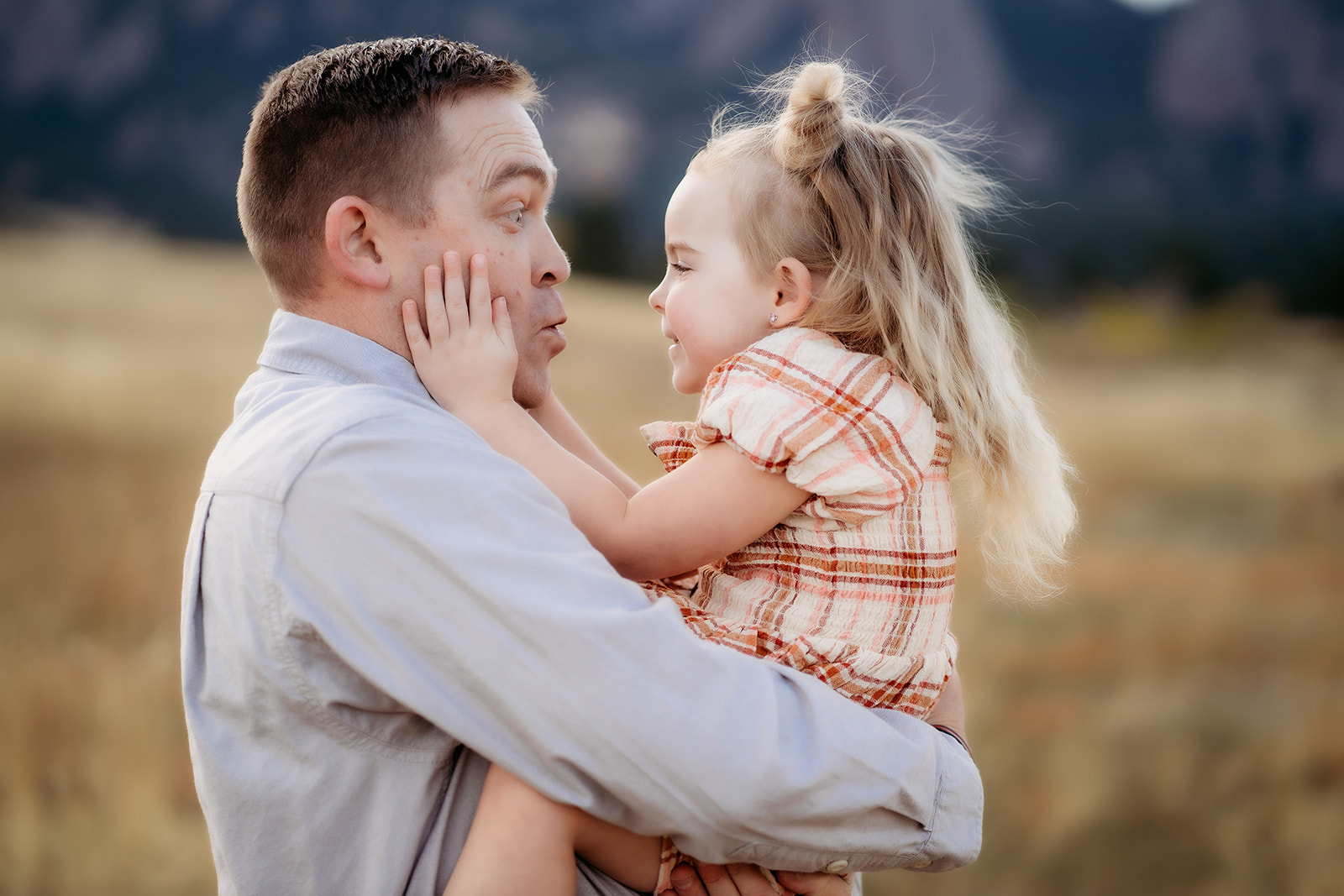 Close-up of father holding his daughter, both laughing as they share a playful moment outdoors.