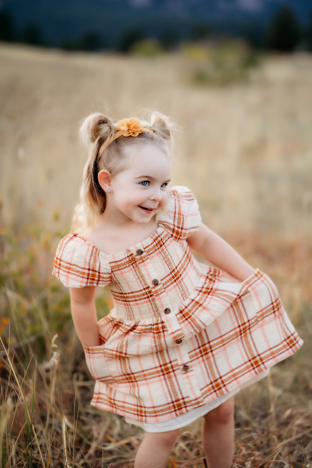 Young girl in a plaid dress smiling shyly with hands in her pockets during family photos Denver.