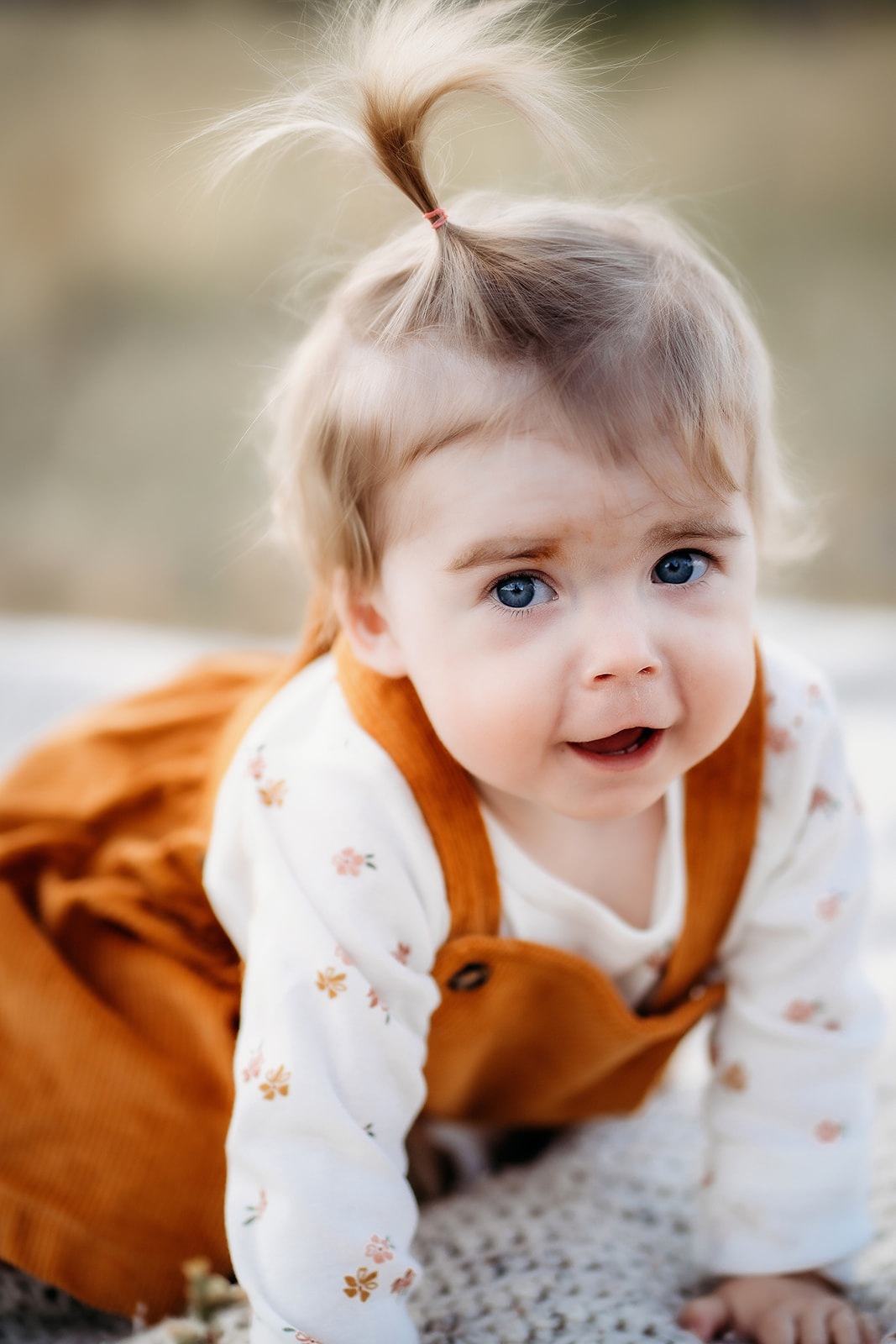 Close-up of a baby in a rust-colored dress crawling on a blanket outdoors in a Colorado meadow.