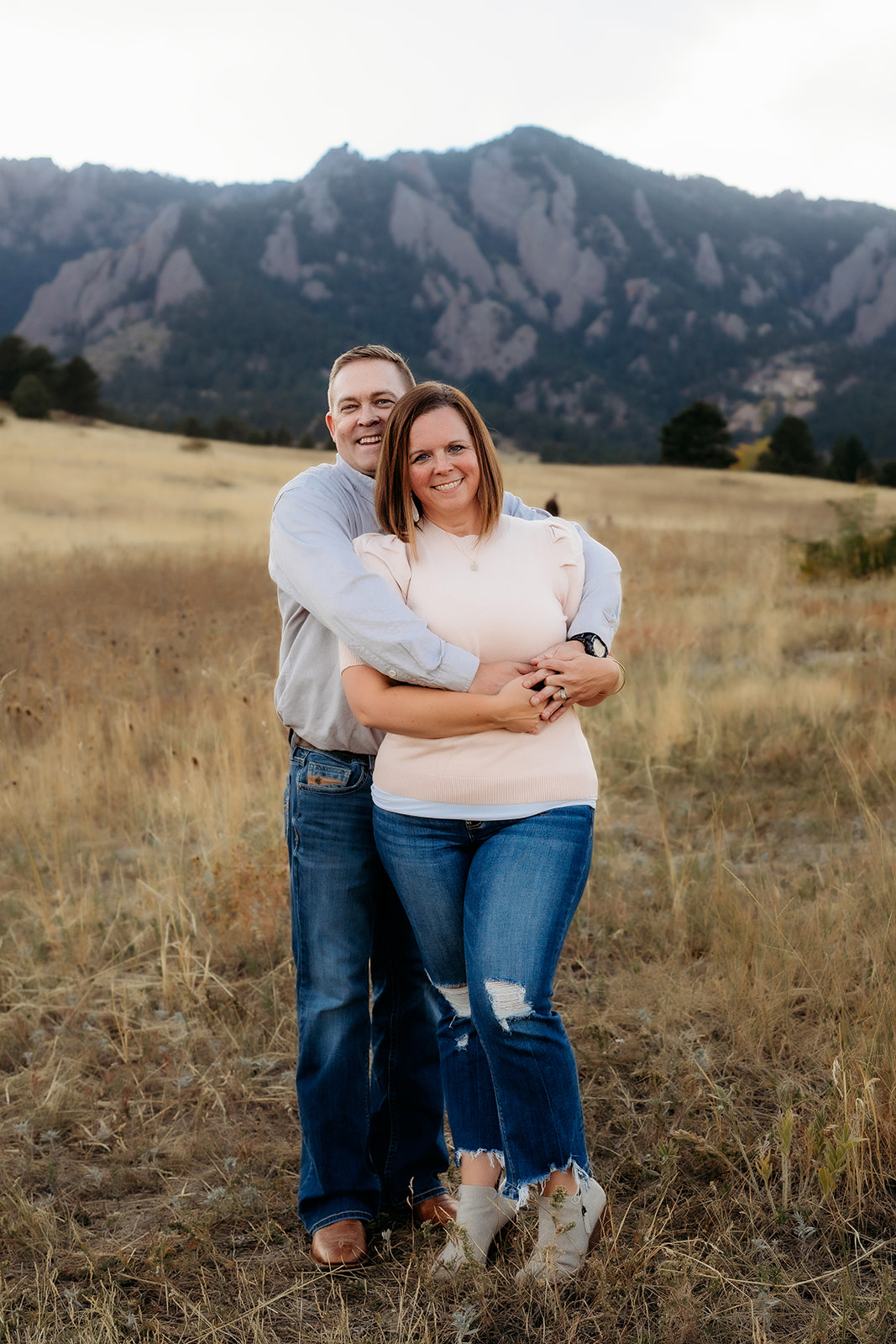 Couple embracing in a golden Colorado field with the Flatirons in the background during family photos Denver.