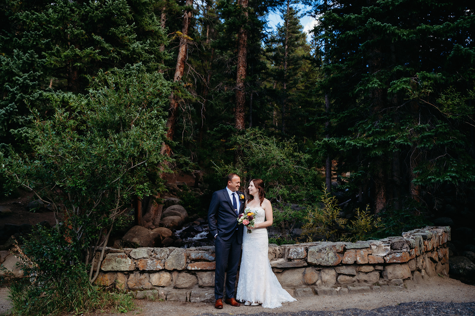 Sharing a private smile in front of a stone wall and mountain stream, this couple soaks in their elopement in Colorado.