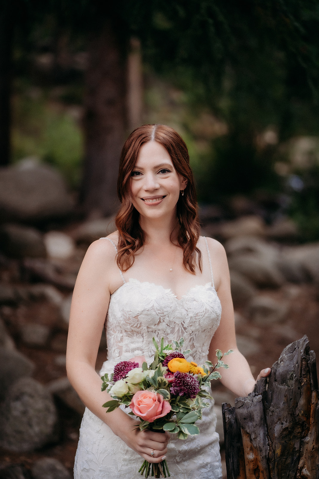 Holding a colorful bouquet, the bride stands glowing in the forest light—ready for her elopement in Colorado.