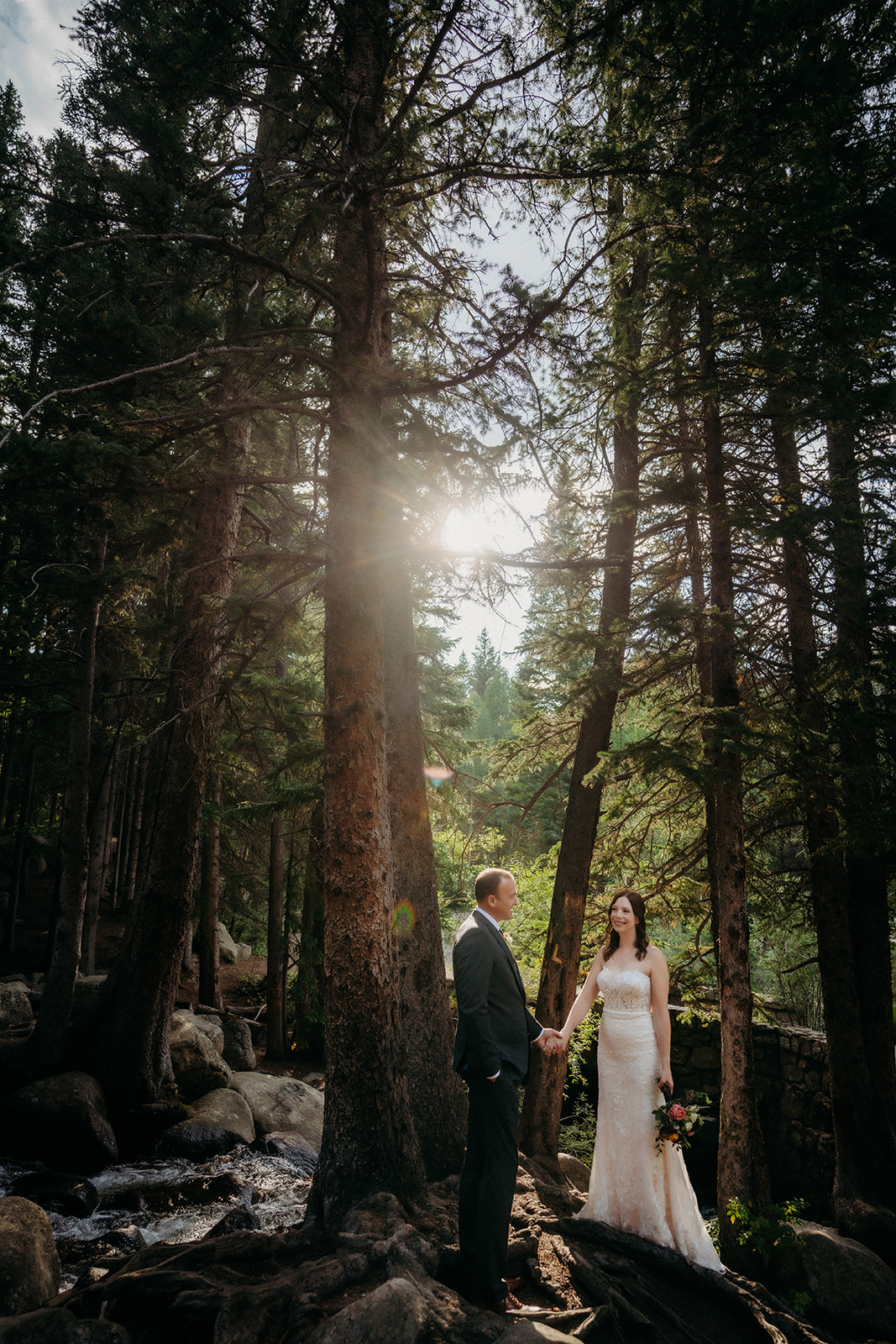 In the forest with sunbeams filtering through the trees, the couple pauses hand in hand during their elopement in Colorado.