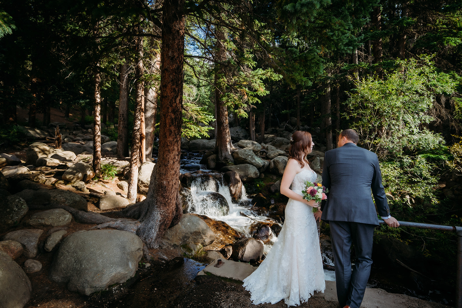 Overlooking a cascading creek, the couple pauses to take in the beauty of nature during their elopement in Colorado.
