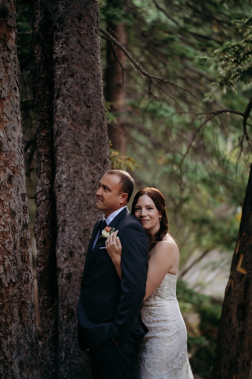 Tucked between tall trees, the bride wraps her arms around the groom during a quiet moment alone.