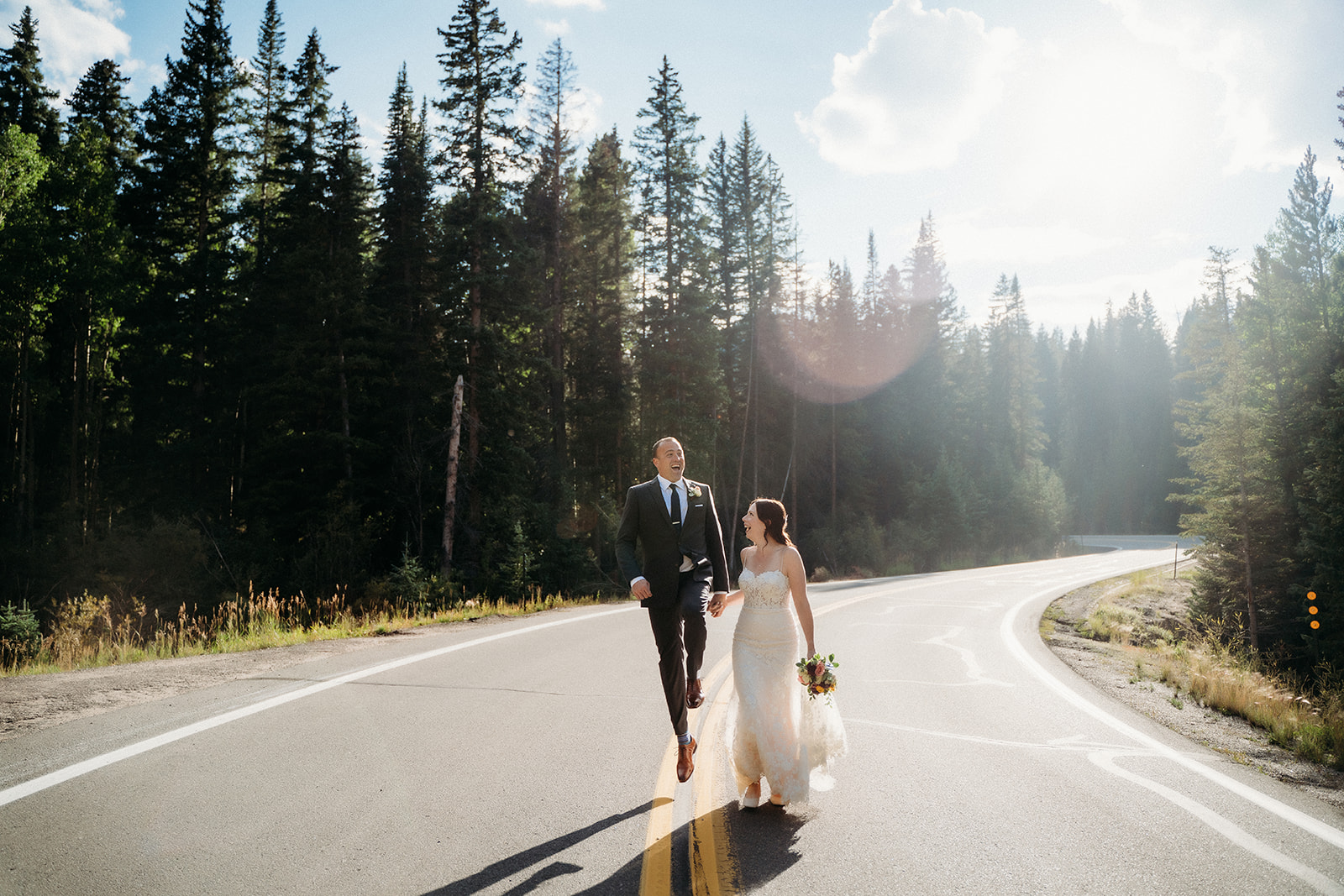 The couple walks down a winding mountain road, hand in hand, sunlight streaming through the pine trees.