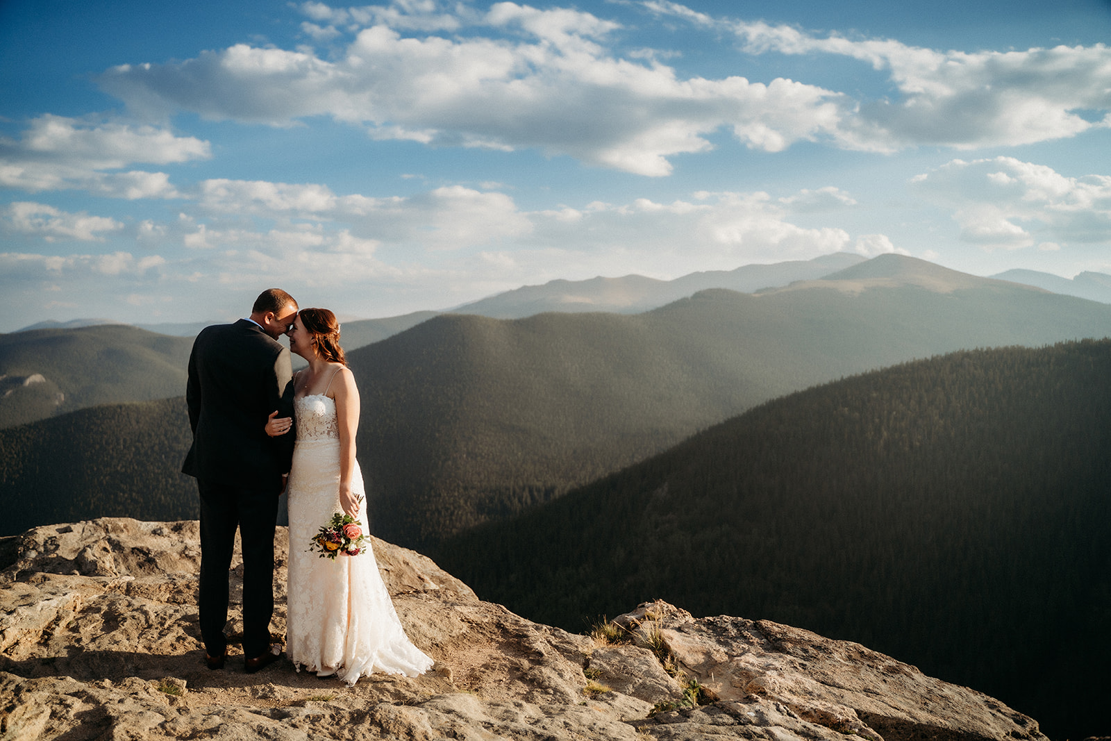 A gentle kiss on the forehead while standing at the edge of a mountaintop captures the stillness of their love.