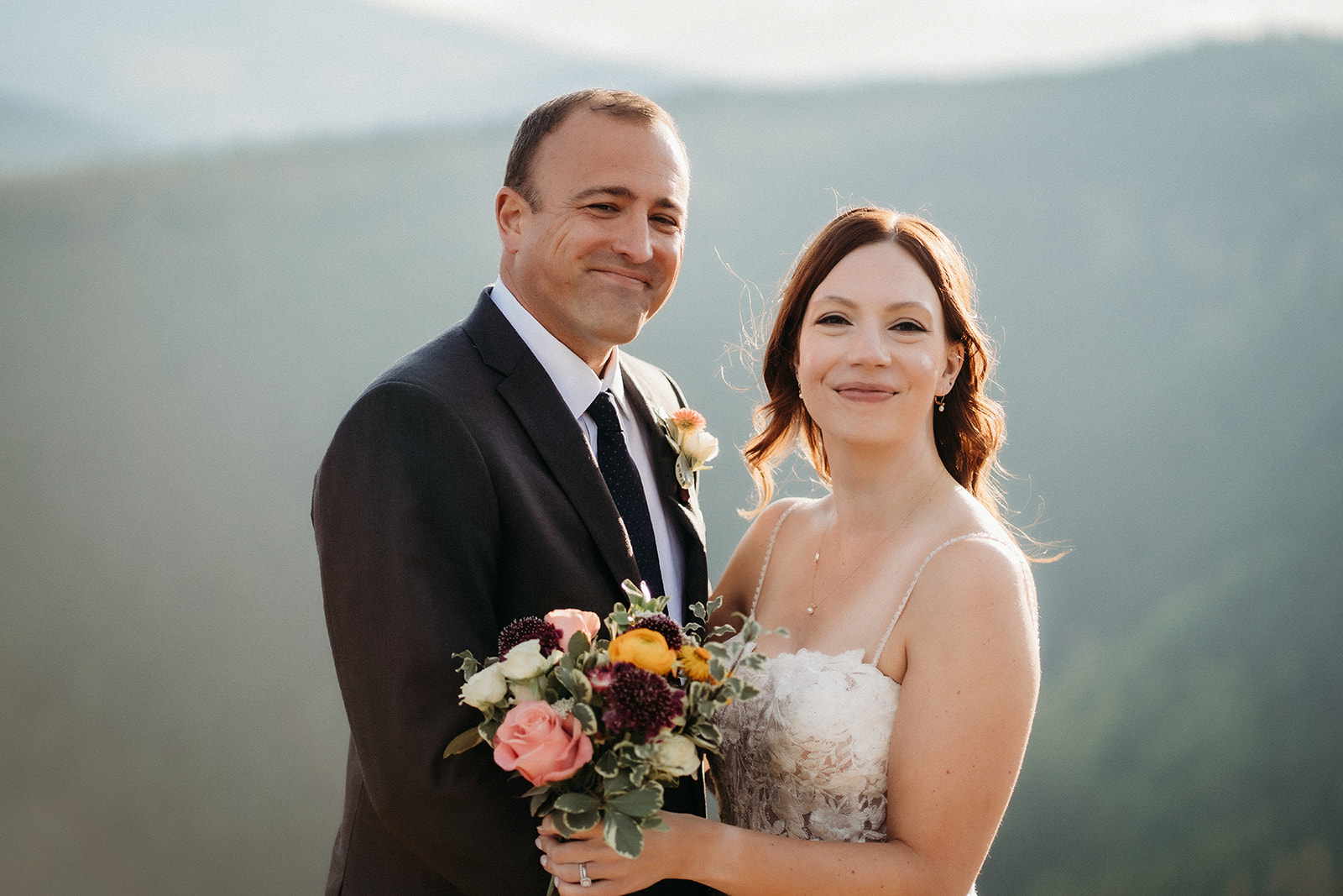Smiling softly for the camera, the couple stands close with the afternoon sun glowing around them.