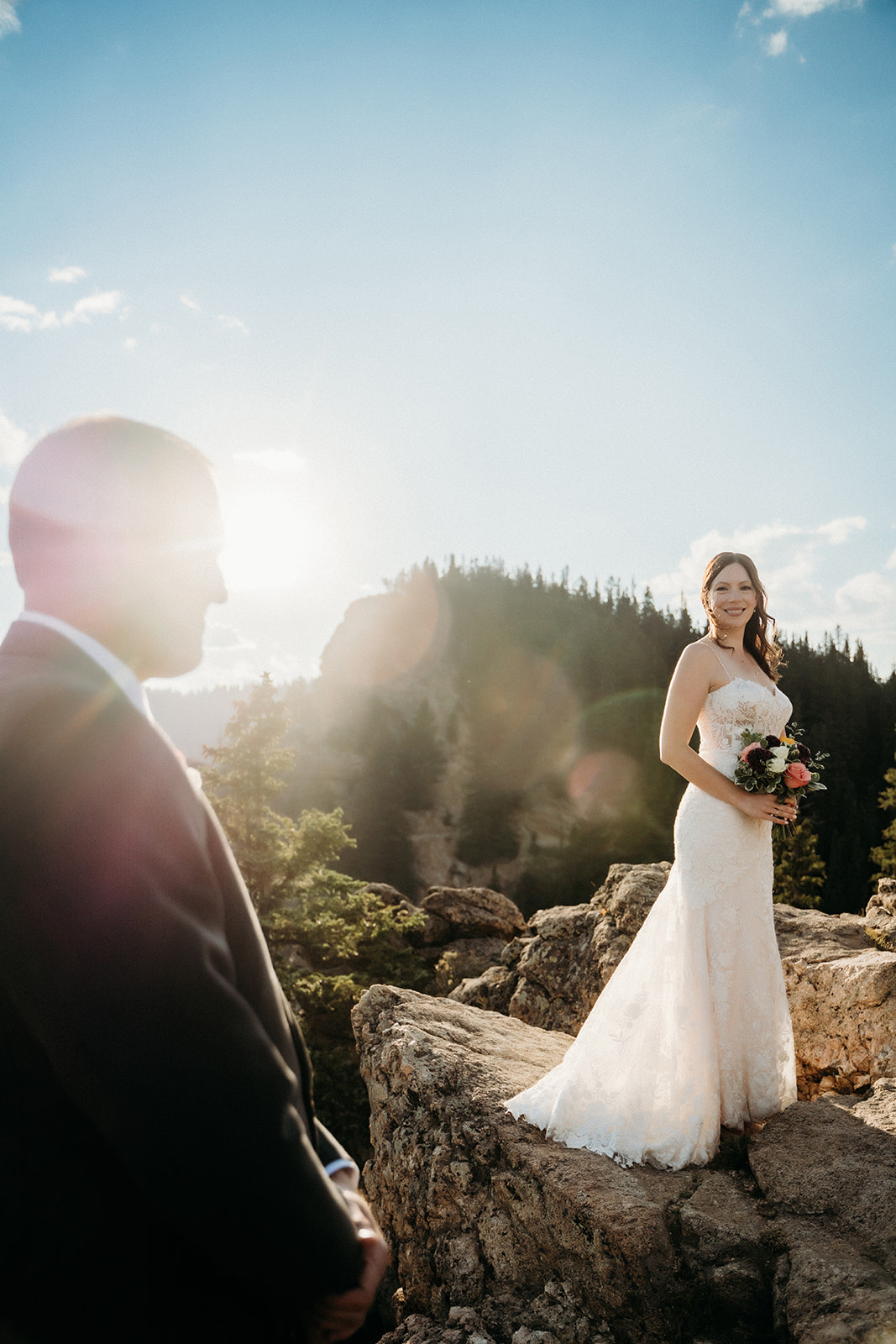 The groom watches lovingly as the bride smiles in soft golden light on a scenic overlook.