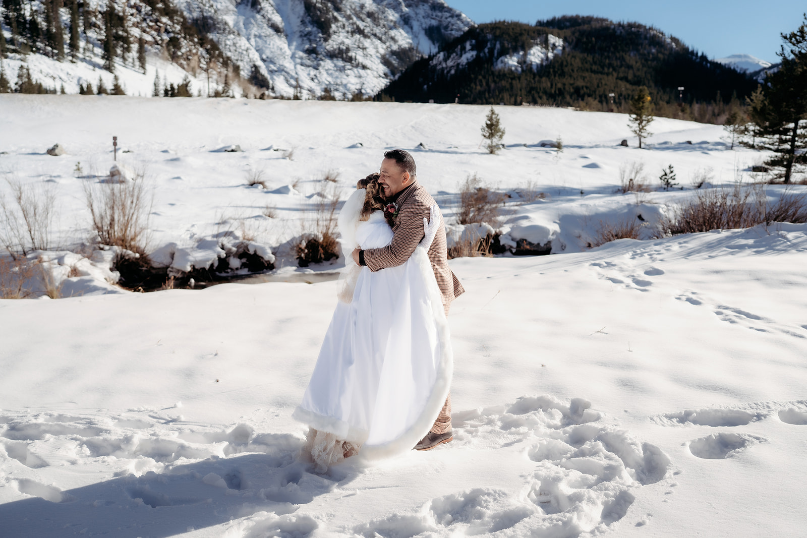 Groom lifts the bride in a joyful embrace in an open, snow-covered field during their winter elopement in Colorado.