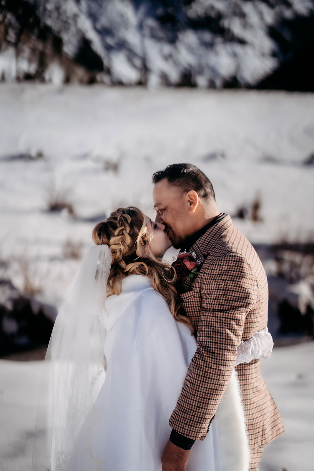 Bride and groom kiss under the winter sun, wrapped in a white cape and warm love during their Colorado elopement.
