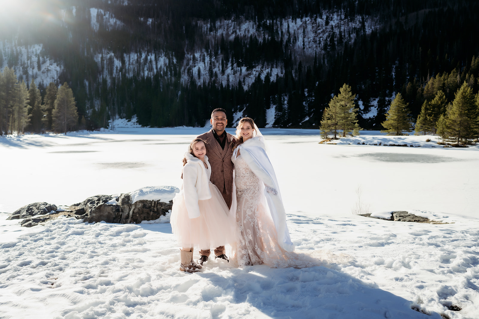 Family photo of bride, groom, and daughter standing together in the snow during their winter elopement in Colorado.