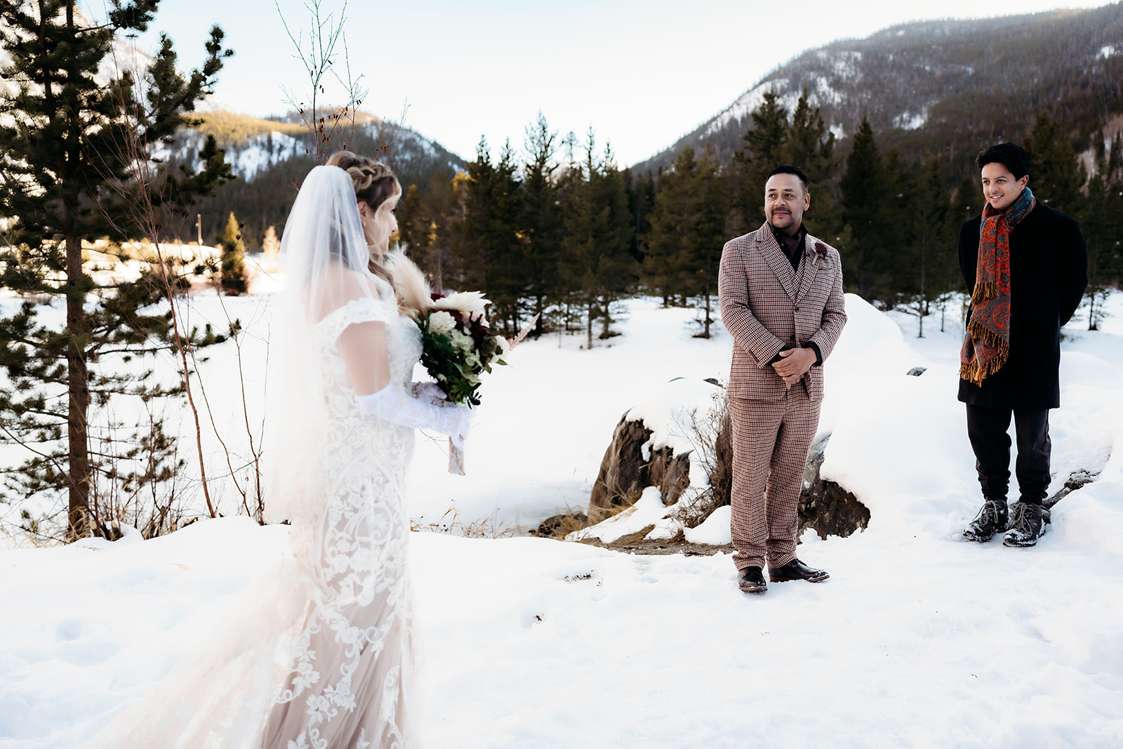 Bride walks toward the groom with a bouquet in hand, both smiling during a snowy first look moment.