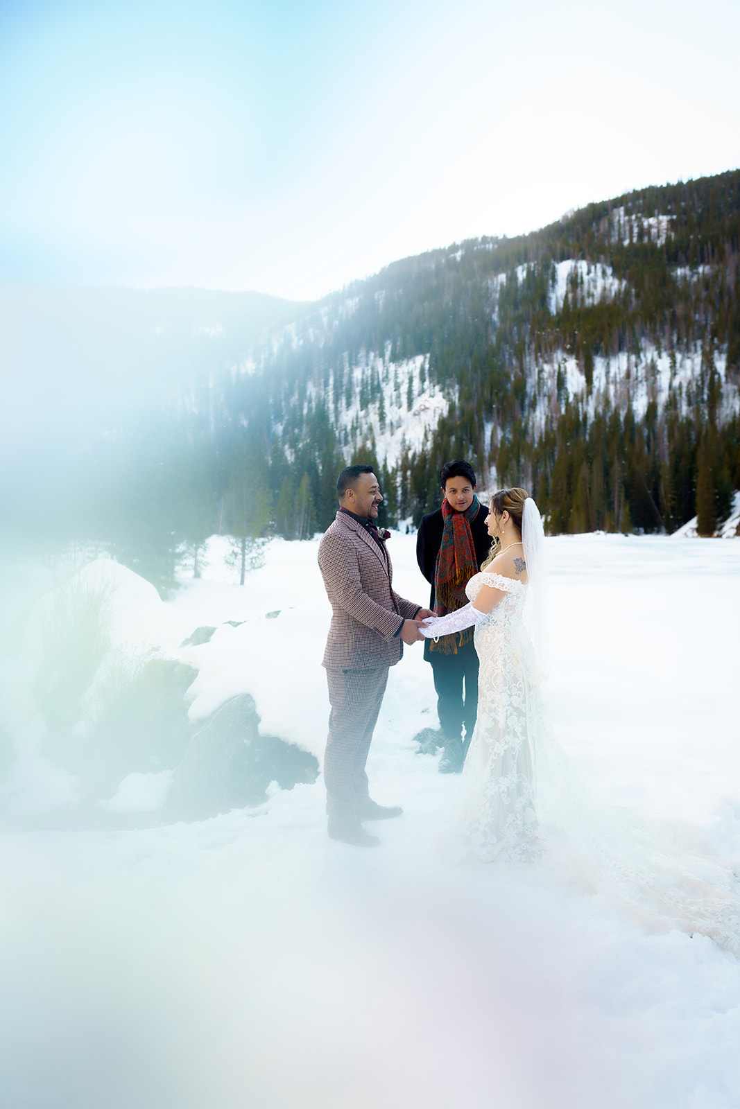 Couple exchanges vows in front of an officiant beside a frozen alpine lake during their winter elopement in Colorado.