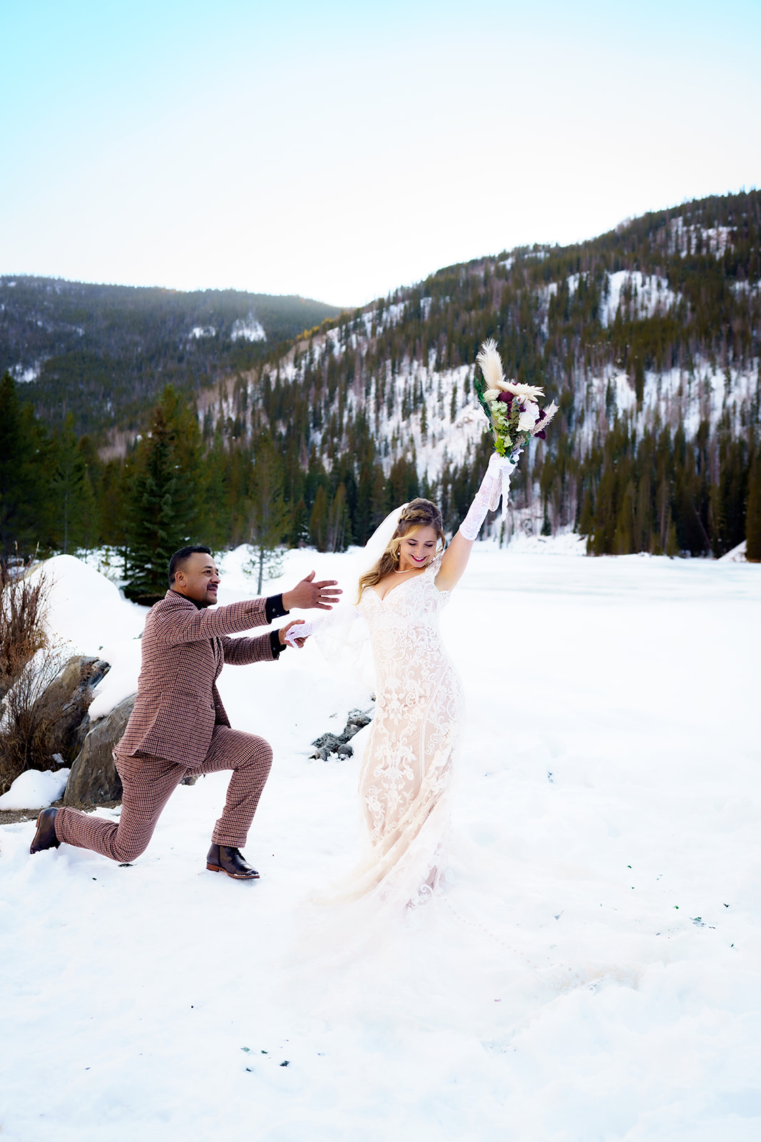 Groom playfully reaches for the bride as she triumphantly raises her bouquet in the air, celebrating their winter elopement in Colorado.
