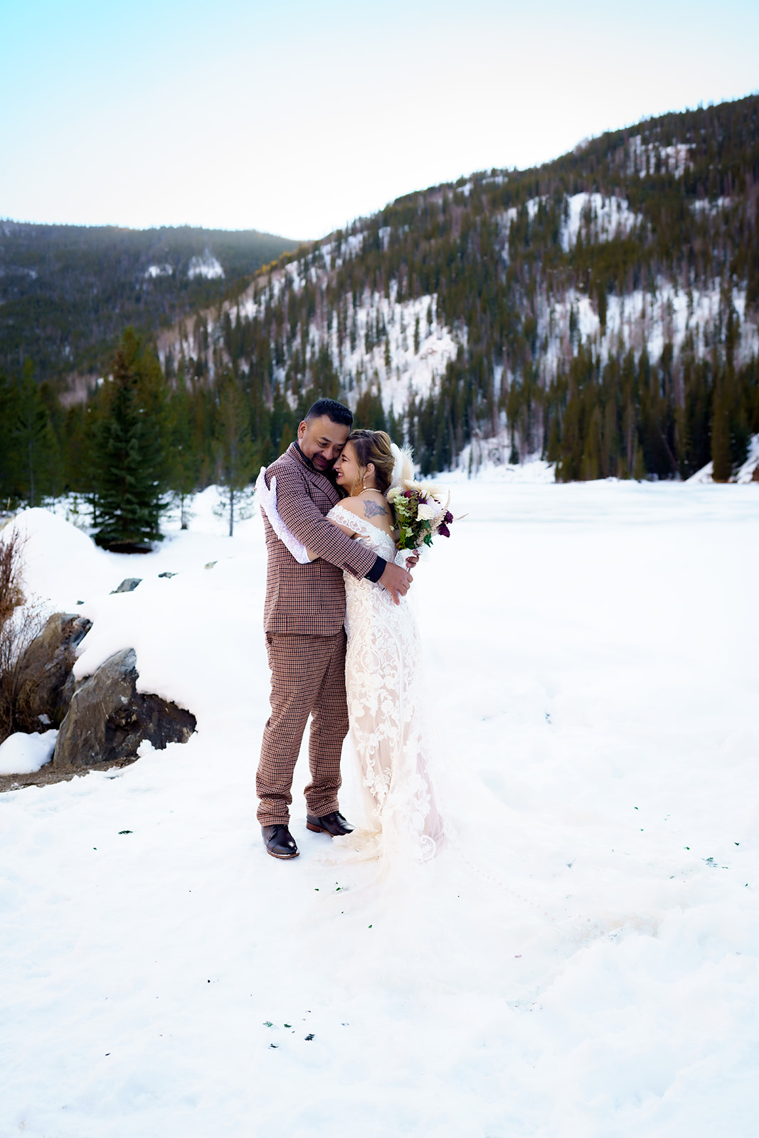 Couple shares a quiet embrace beneath the trees, surrounded by snow and the peaceful stillness of their elopement day.