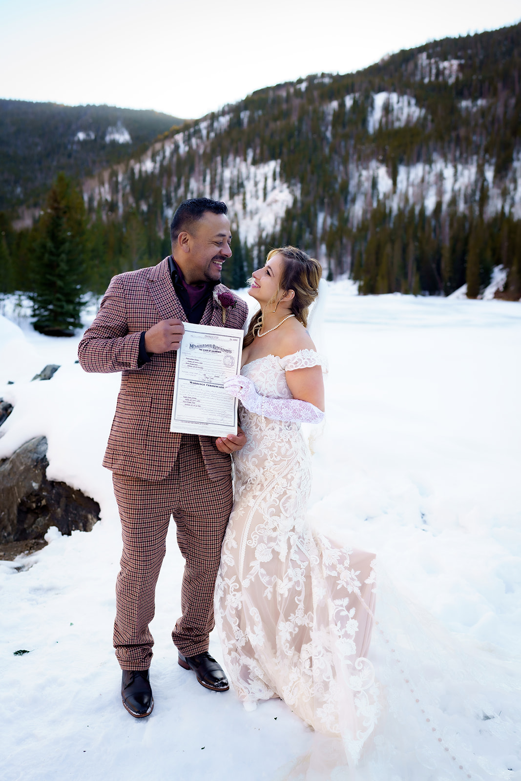 Bride and groom hold up their signed marriage license, beaming with joy during their winter elopement in Colorado.