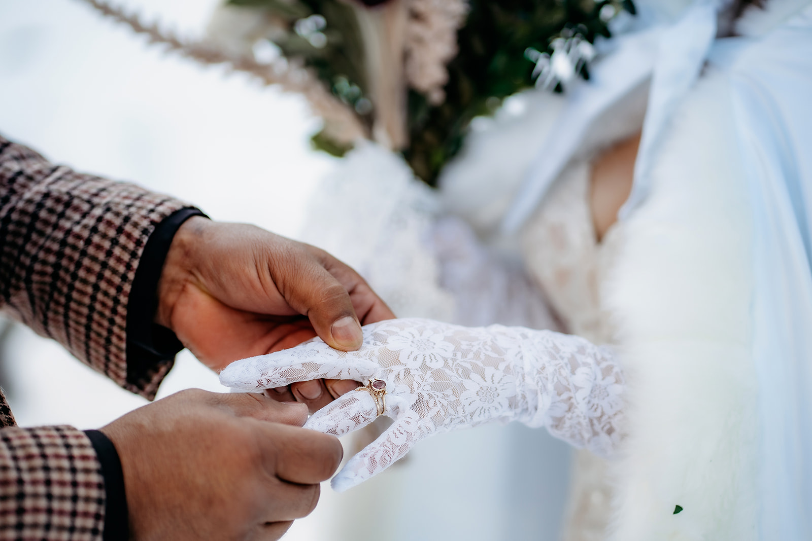 Groom gently places the wedding band on the bride’s lace-gloved finger during their snowy ceremony.