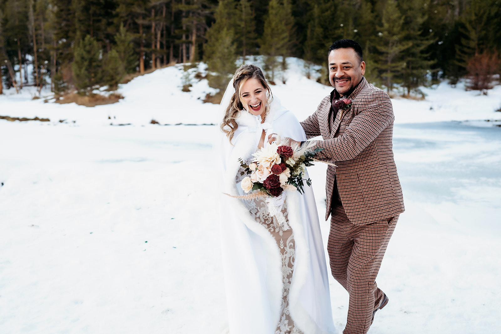 Bride and groom laughing joyfully as they walk together through the snowy forest during their winter elopement in Colorado.