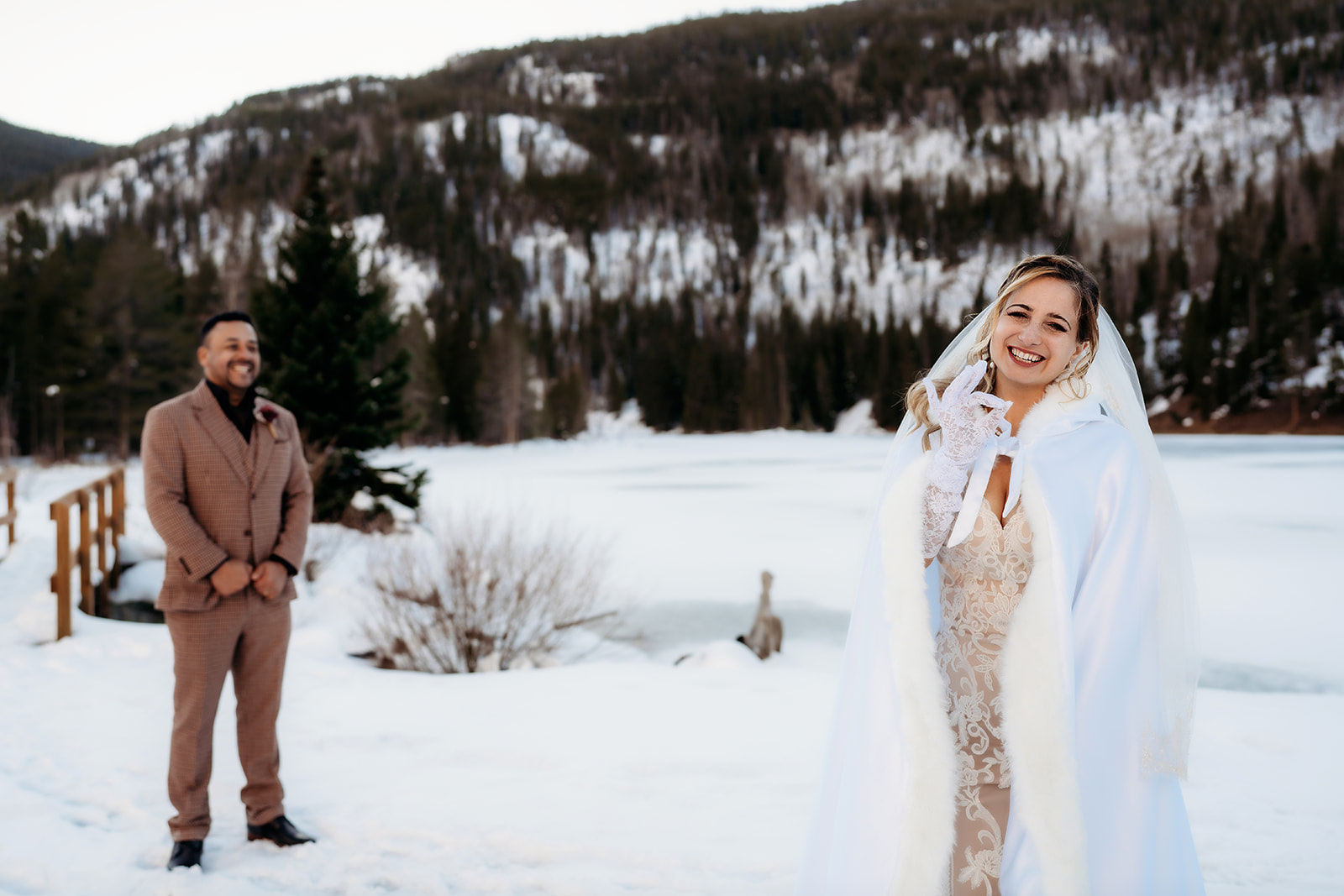 Bride turns to smile at the groom during a private moment before their ceremony, a frozen alpine lake behind them.