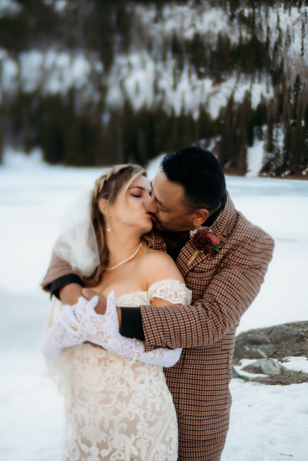 Bride and groom share a kiss during their winter elopement in Colorado, wrapped in each other’s arms beside a frozen alpine lake.