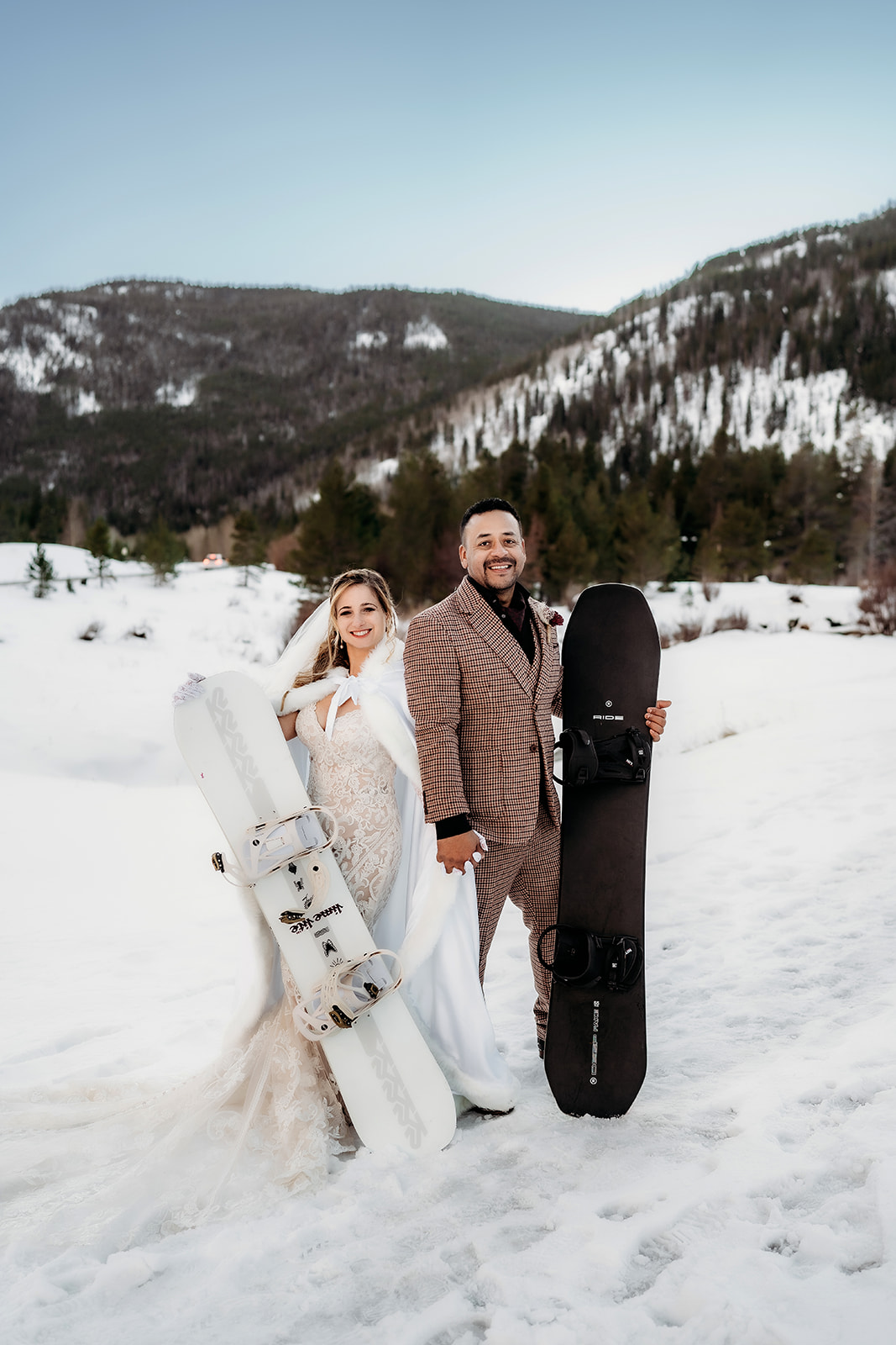 Adventurous couple poses with snowboards, smiling after their winter elopement in Colorado’s snowy mountain landscape.