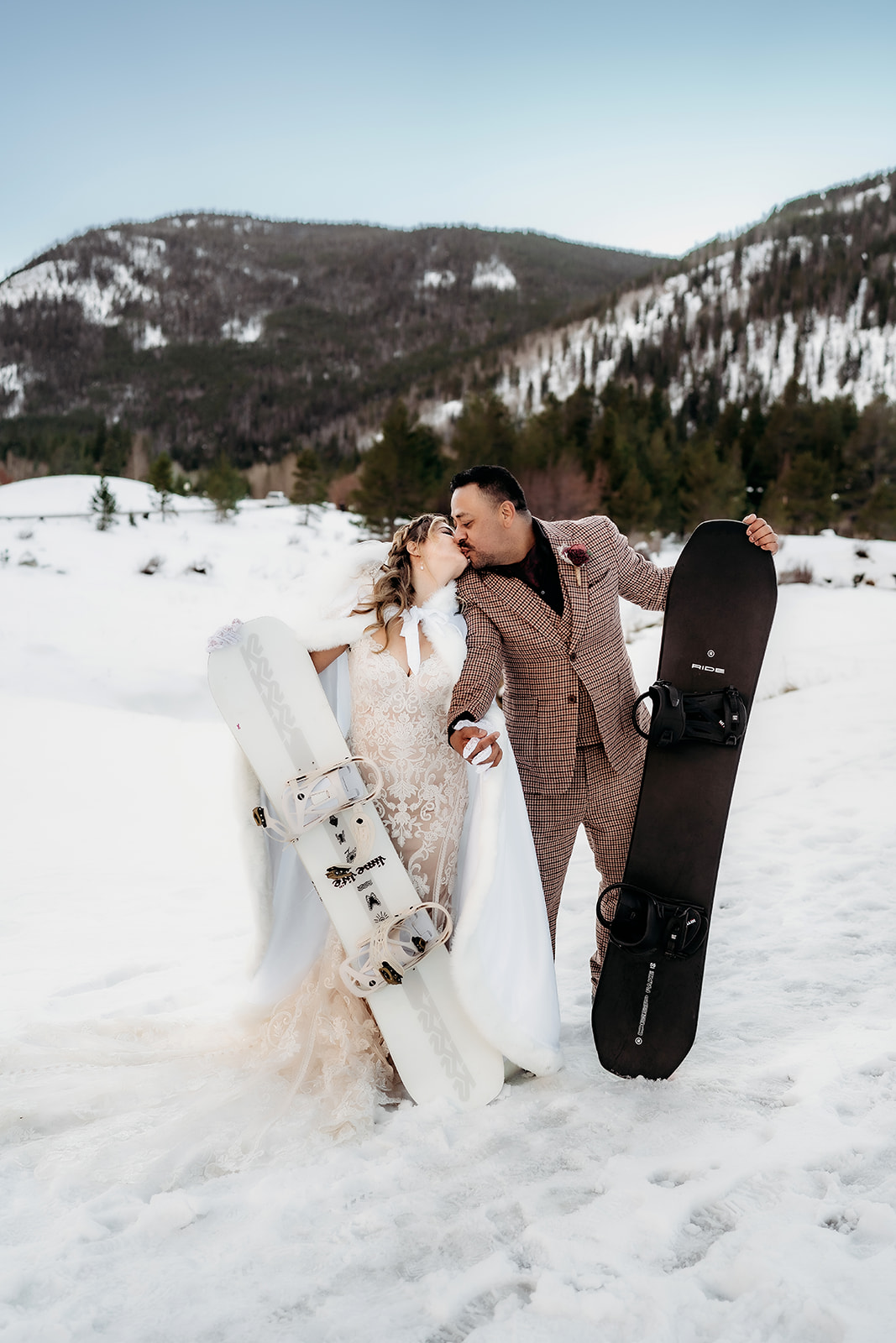 Couple kisses in the snow while holding their snowboards, celebrating their adventurous winter elopement in Colorado.