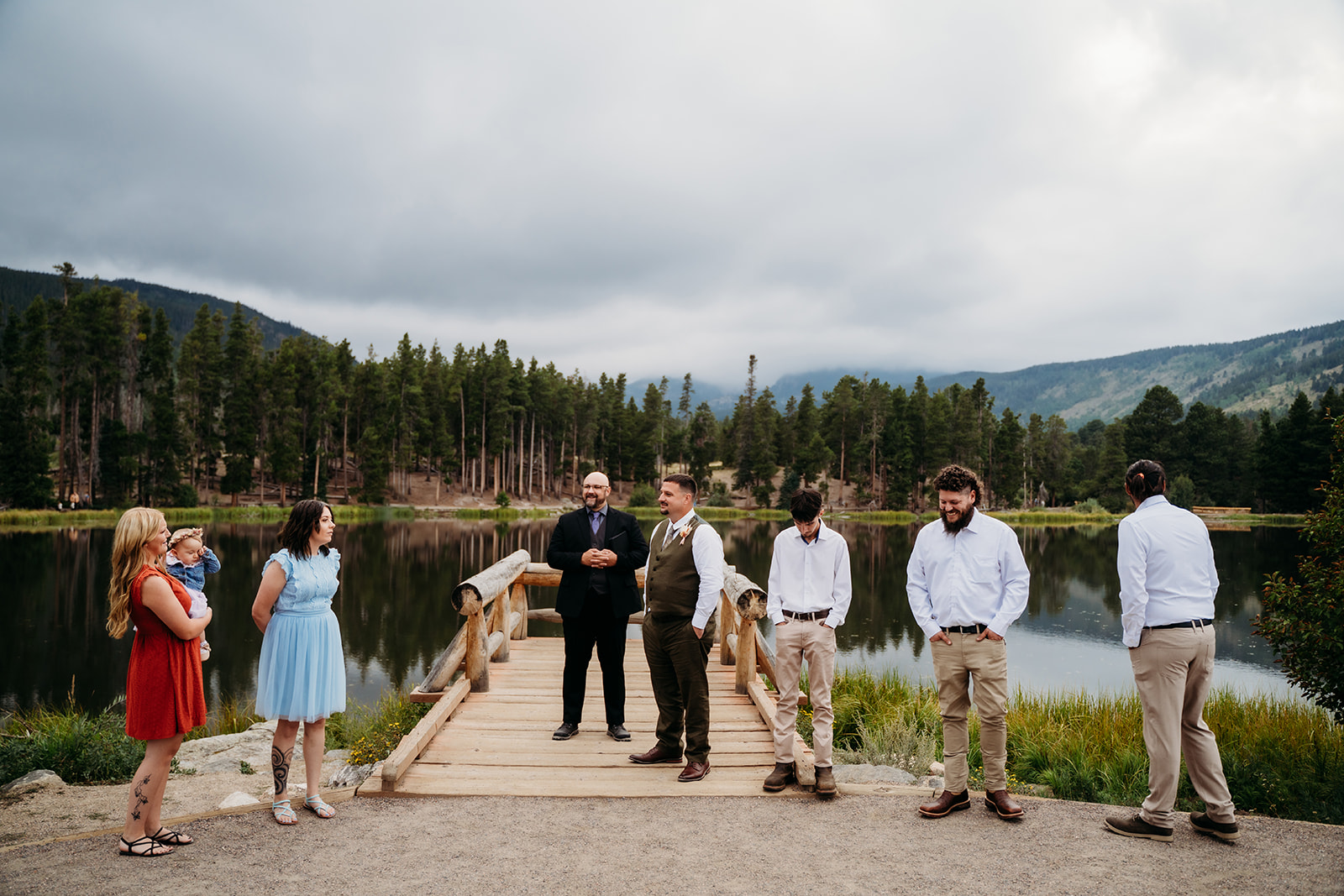 Guests gather casually at the edge of a mountain lake, waiting for the ceremony to begin at this intimate wedding.