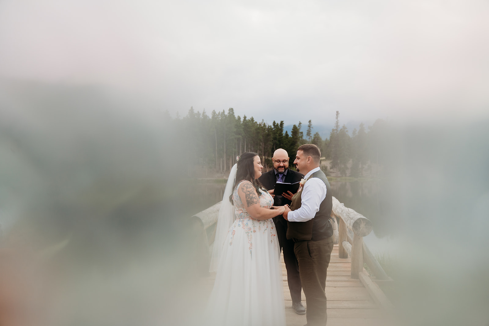 Bride and groom hold hands and smile at each other, framed by soft, romantic blur during their intimate wedding.