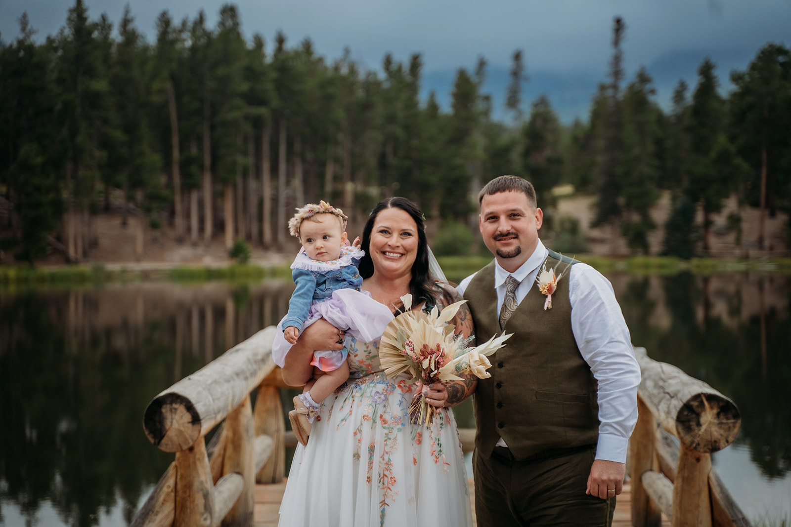 Bride and groom smile with their baby girl and bouquet in hand after their heartfelt intimate wedding ceremony.