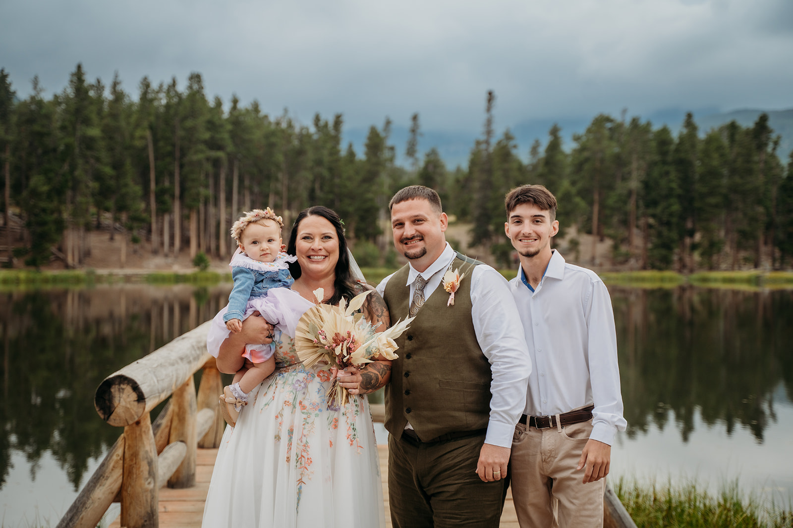 Family portrait with the bride, groom, their baby daughter, and teenage son on the dock, all beaming after the ceremony.