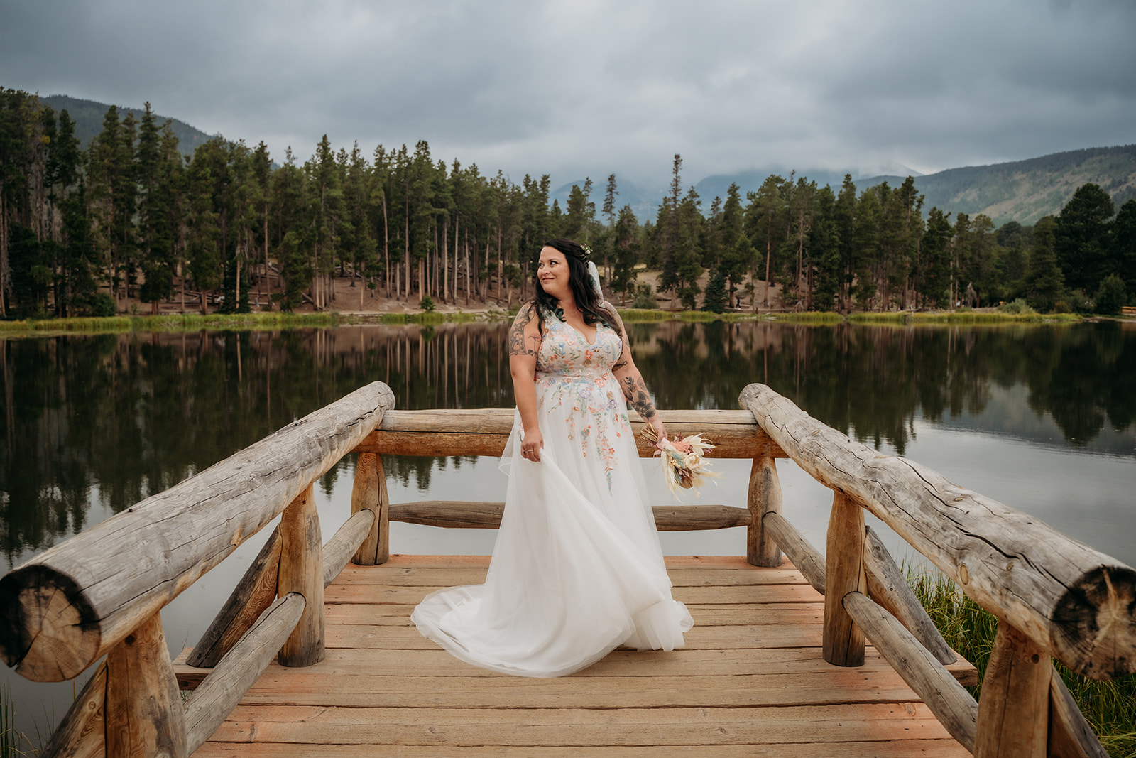 Bride twirls slightly in her gown while standing on the dock, surrounded by calm water and towering evergreens.