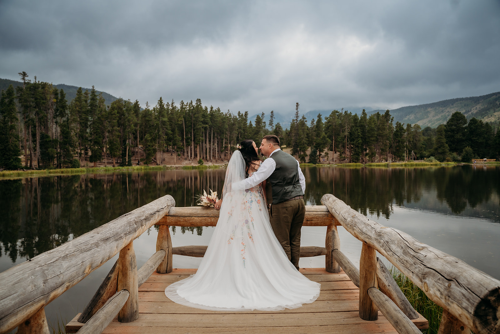 Couple shares a kiss while looking out over a still lake, celebrating their intimate wedding with a quiet moment alone.