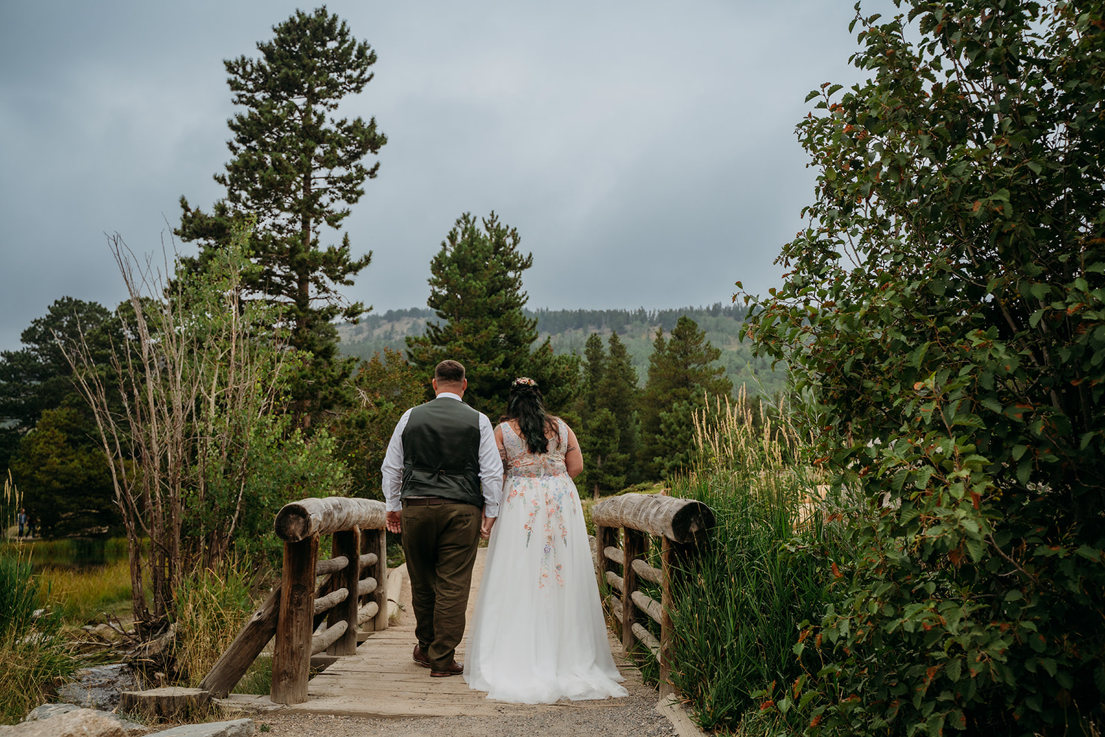 Couple walks away across a wooden bridge hand-in-hand, the lush forest surrounding them on their intimate wedding day.