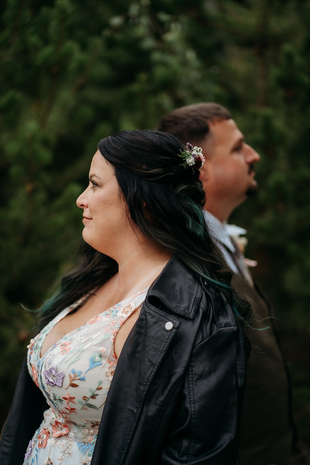 Bride and groom stand back to back in front of pine trees, capturing a creative portrait after their intimate wedding.
