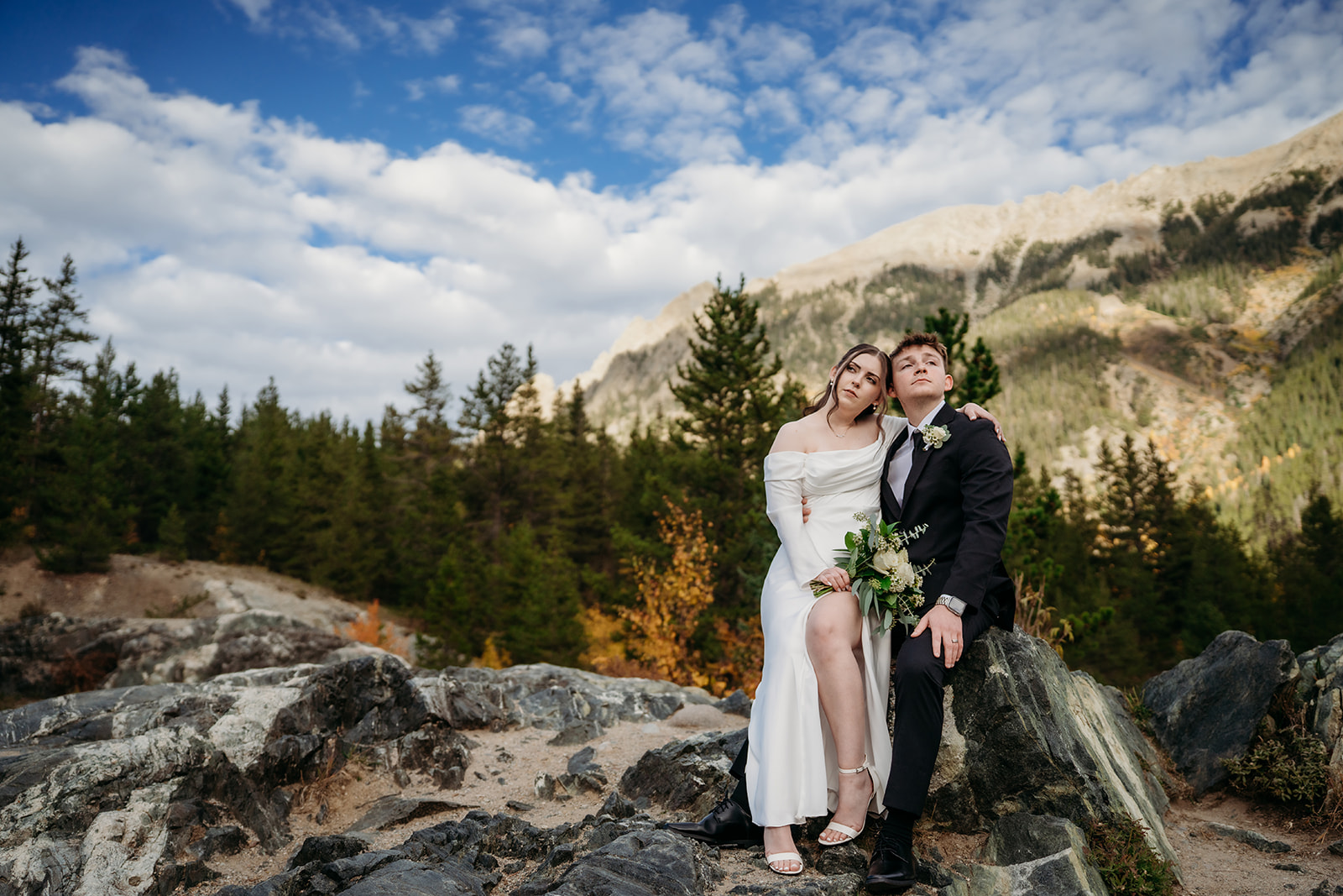 Sitting together on a boulder, the bride leans into her groom as they breathe in the crisp mountain air.