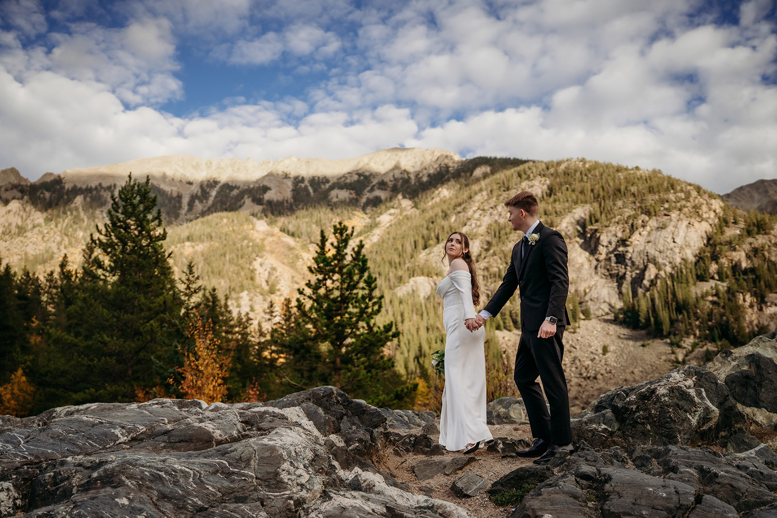 Hand in hand on a rocky overlook, the couple soaks in sweeping mountain views after choosing to elope to Colorado.