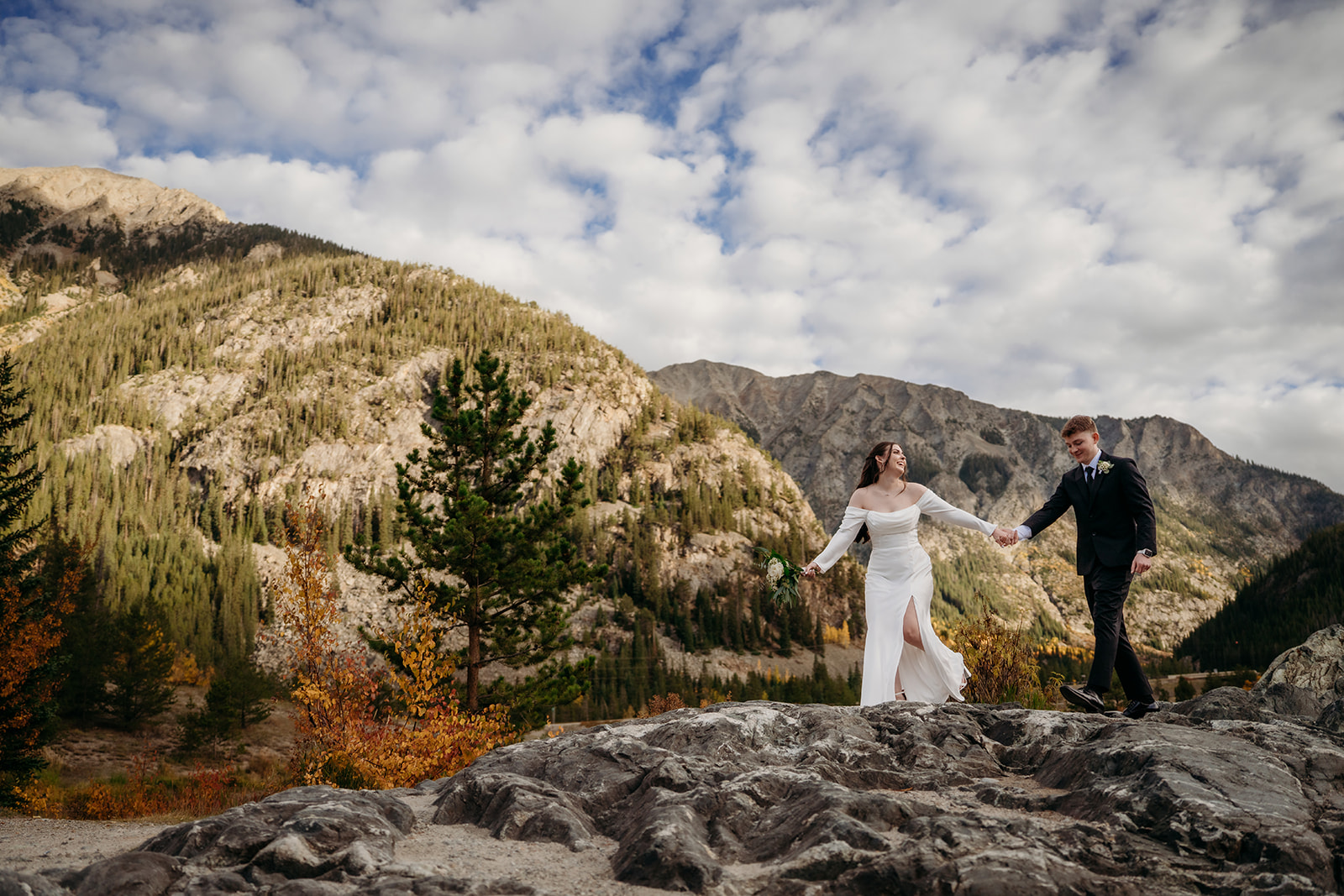 Newly married couple walking across rocky cliff together hand in hand