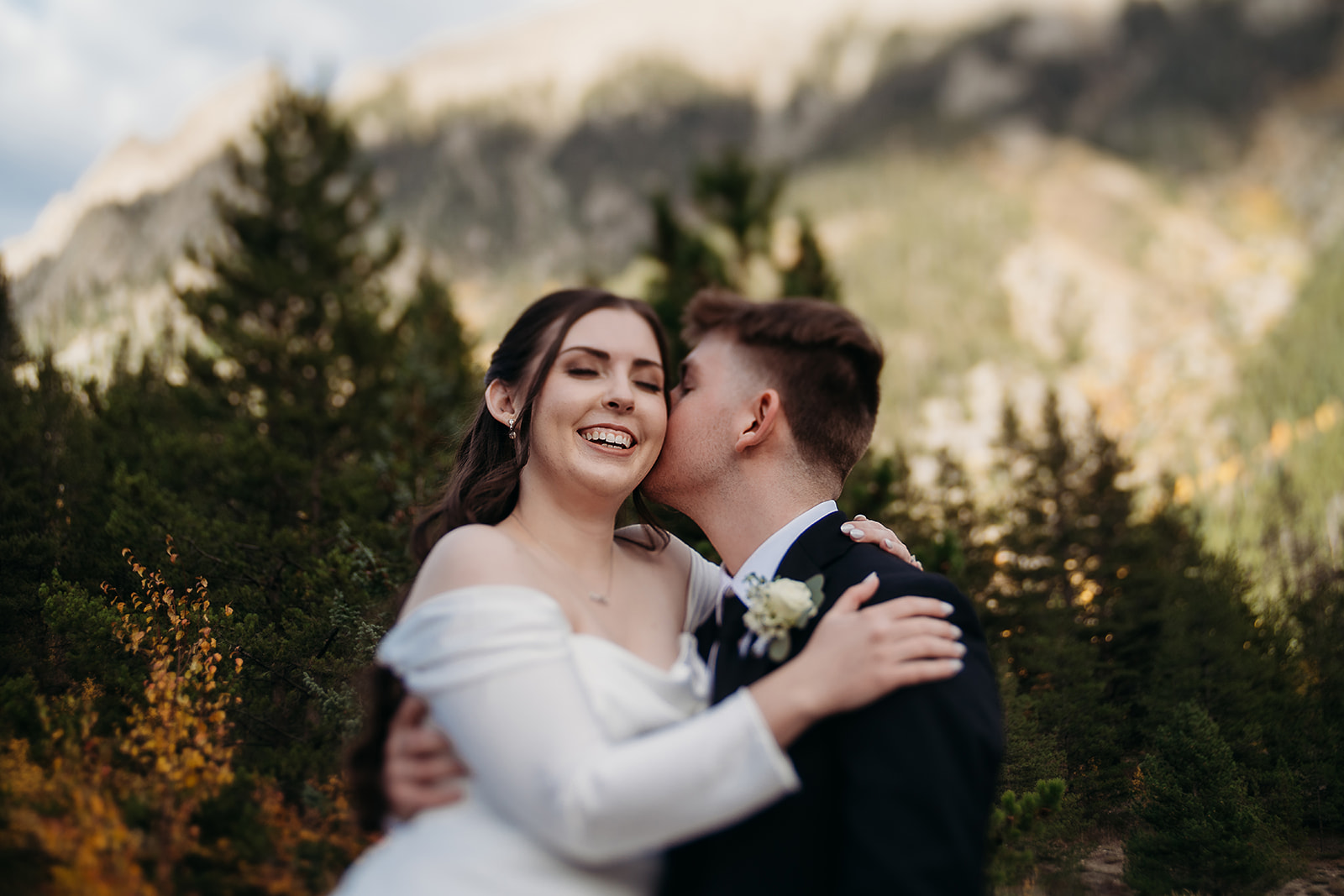 With a kiss on the cheek, the groom makes his bride laugh, surrounded by the wild beauty of the Rockies.