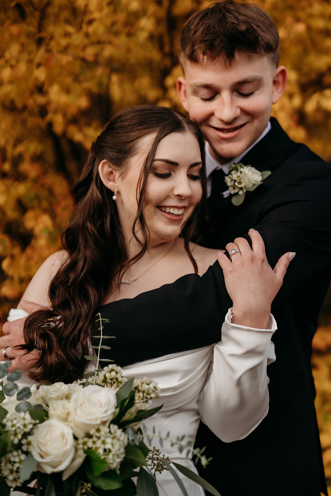 Wrapped in his arms, the bride smiles down at her bouquet of white roses during their golden-hour photo session.