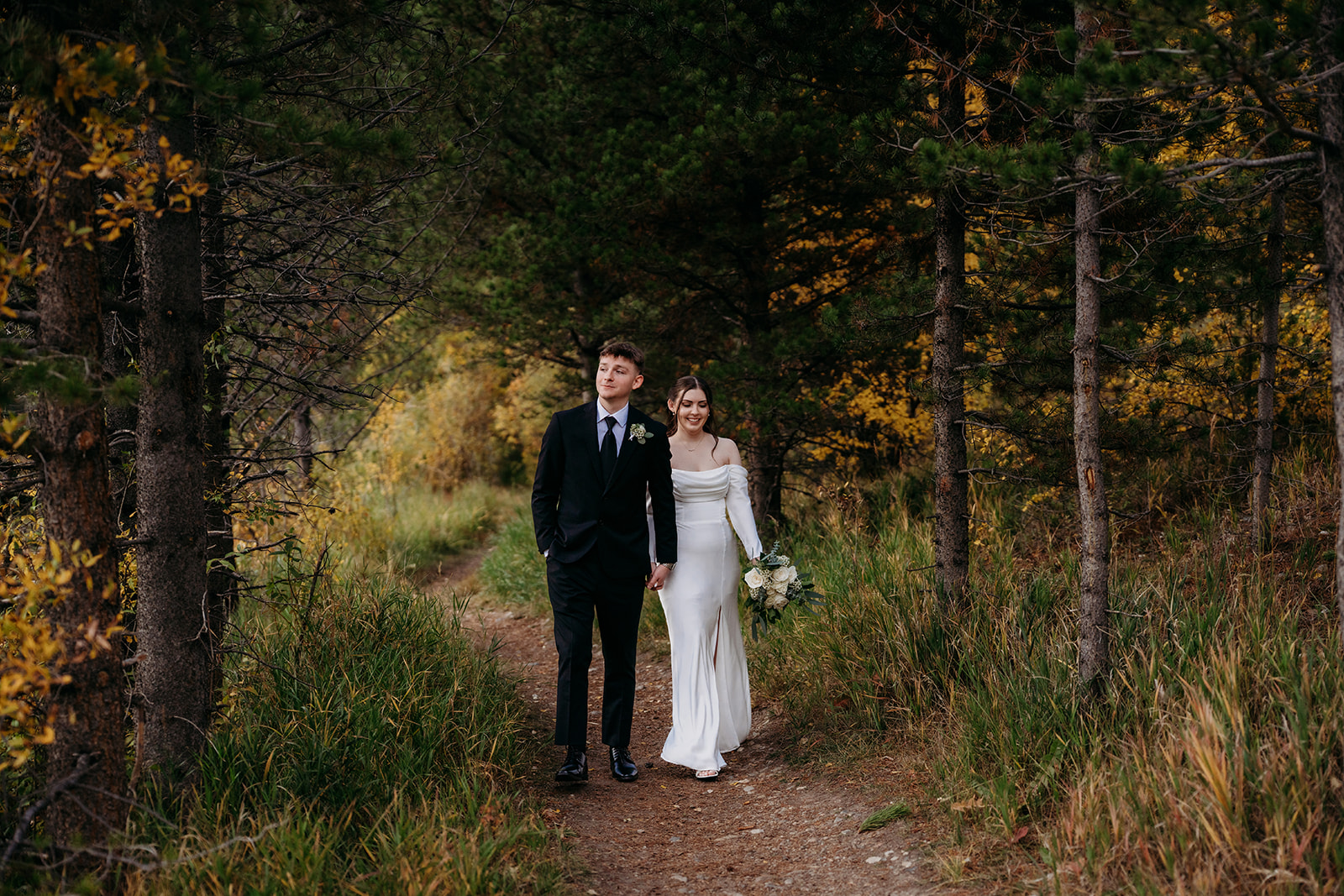 Newly married couple walking hand in hand through forest after they elope to Colorado
